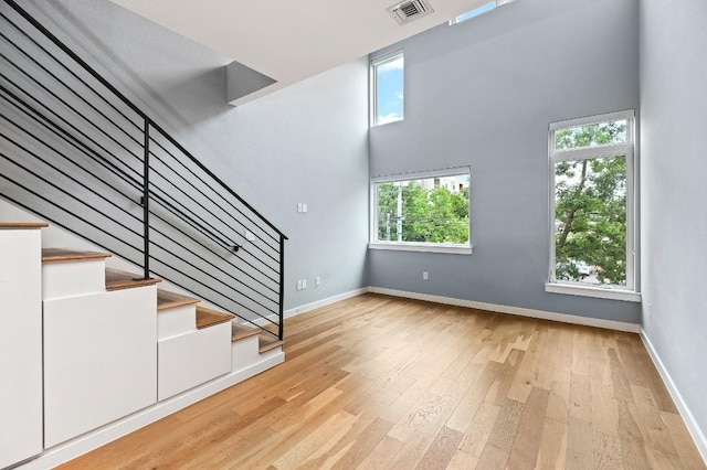 2002 E 7th St Unit 204, Austin, TX 78702 - unfurnished living room with stairs, light wood finished floors, baseboards, and a towering ceiling
