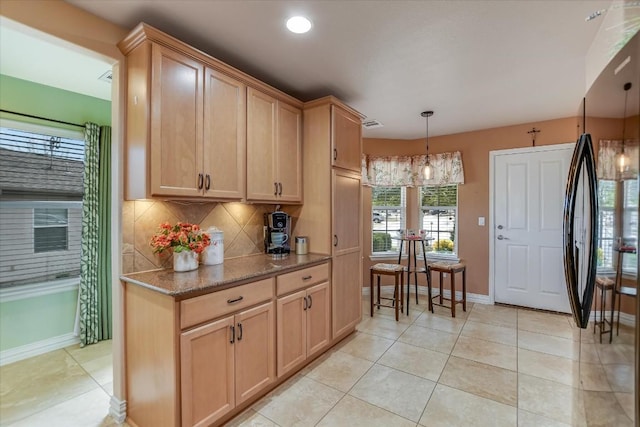 kitchen with light tile patterned floors, backsplash, black fridge, light brown cabinets, and hanging light fixtures