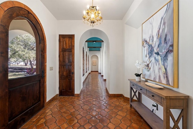 foyer entrance with baseboards, arched walkways, a notable chandelier, and stone finish flooring