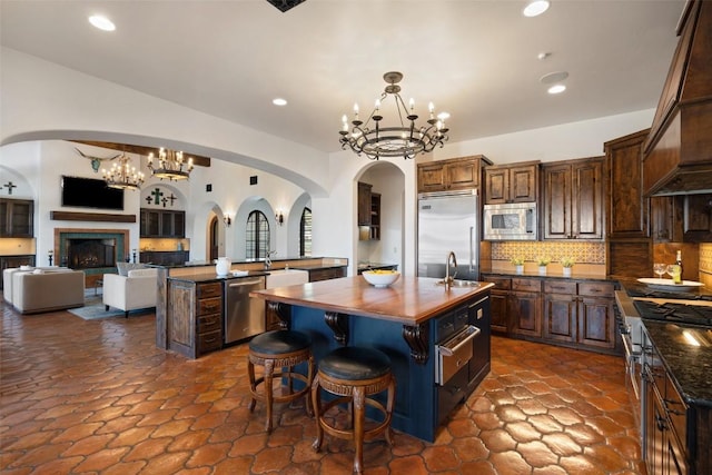 kitchen featuring arched walkways, built in appliances, an inviting chandelier, and an island with sink