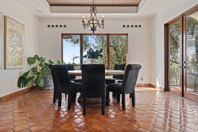 dining area featuring a raised ceiling, an inviting chandelier, and baseboards