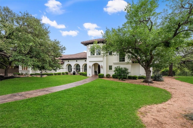 mediterranean / spanish home with stucco siding, a tiled roof, and a front lawn