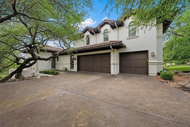 mediterranean / spanish-style house featuring a tiled roof, concrete driveway, and stucco siding