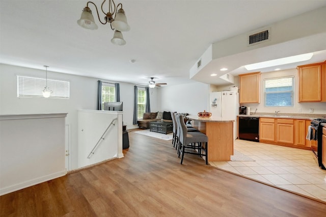 kitchen with black appliances, decorative light fixtures, a breakfast bar, a kitchen island, and sink