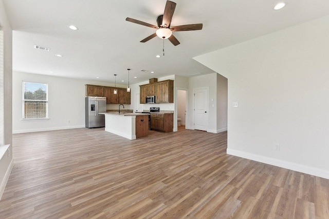 kitchen with light wood finished floors, visible vents, a kitchen island with sink, appliances with stainless steel finishes, and open floor plan