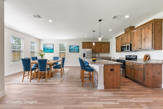kitchen featuring a sink, brown cabinetry, a breakfast bar area, stainless steel appliances, and visible vents