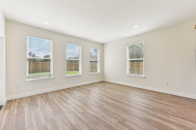 unfurnished room featuring light wood-style flooring, a wealth of natural light, and baseboards