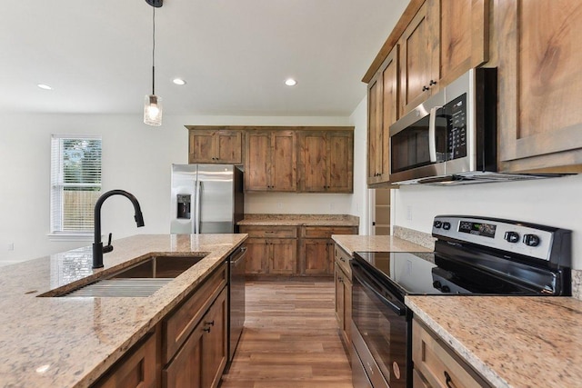 kitchen with wood finished floors, a sink, light stone countertops, pendant lighting, and appliances with stainless steel finishes