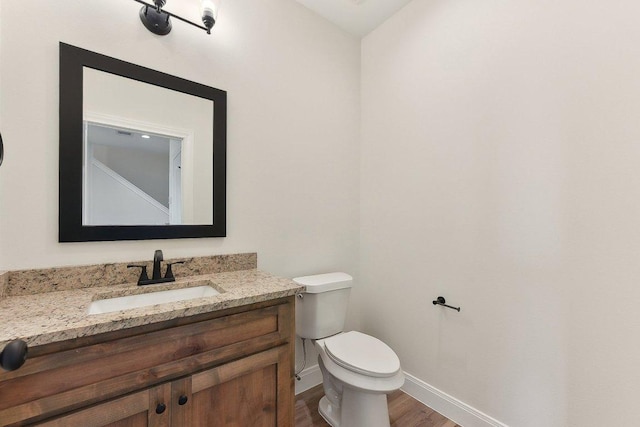 half bath featuring wood finished floors, baseboards, vanity, and toilet