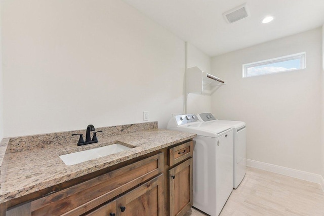washroom with a sink, washing machine and dryer, baseboards, visible vents, and laundry area