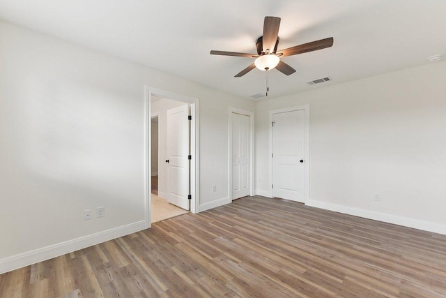 spare room with wood finished floors, visible vents, a ceiling fan, and baseboards