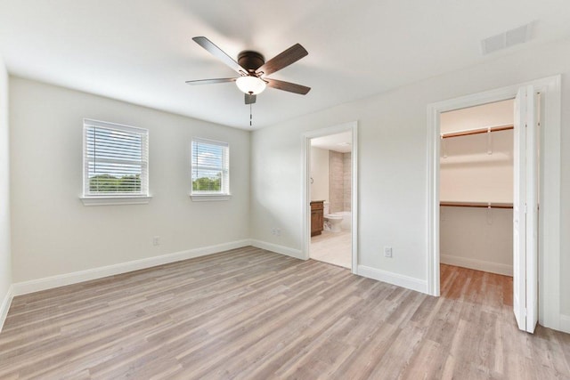 unfurnished bedroom featuring a spacious closet, light wood finished floors, visible vents, connected bathroom, and a closet