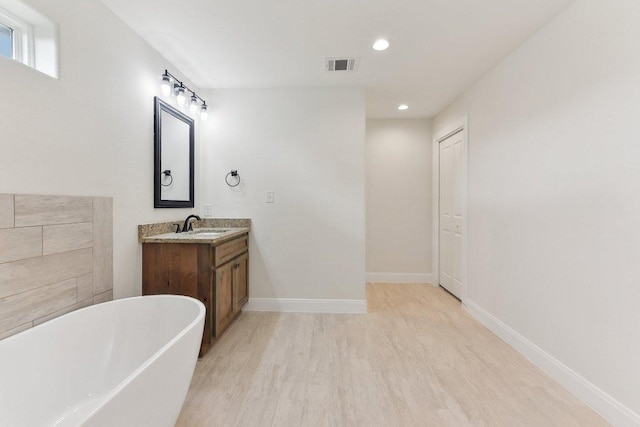 full bathroom featuring recessed lighting, a freestanding bath, wood finished floors, visible vents, and vanity