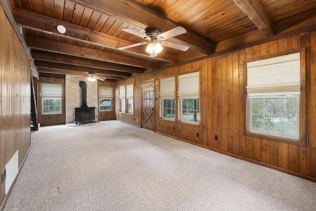 unfurnished living room featuring beam ceiling, wooden ceiling, a wood stove, and a healthy amount of sunlight