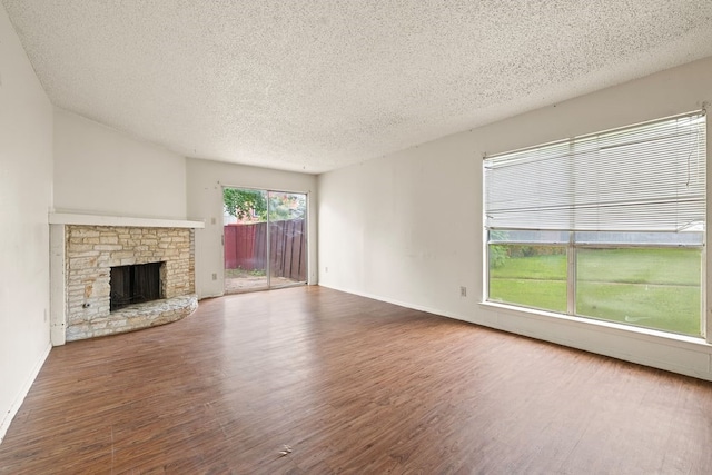 unfurnished living room featuring dark hardwood / wood-style flooring, a stone fireplace, and a textured ceiling