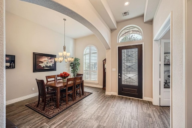 entryway with a wealth of natural light, dark wood-type flooring, vaulted ceiling, and a notable chandelier