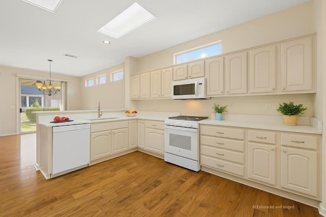 216 Whispering Wind Dr, Georgetown, TX 78633 - kitchen featuring white appliances, a peninsula, light wood-type flooring, a chandelier, and decorative light fixtures