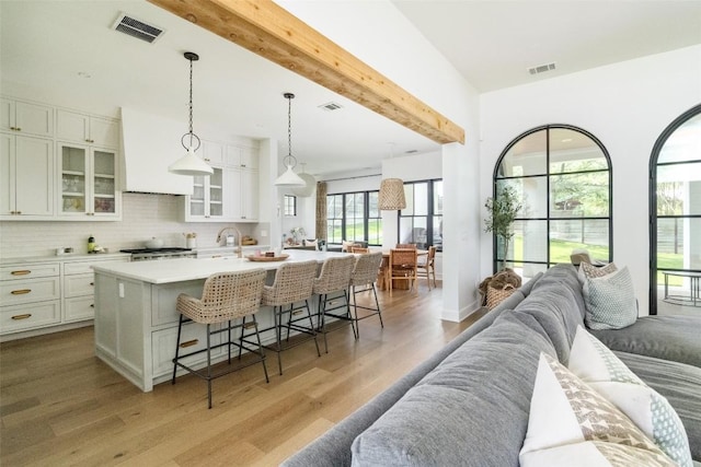 kitchen with backsplash, white cabinets, hanging light fixtures, an island with sink, and a breakfast bar area