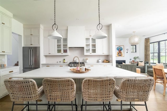 kitchen featuring a center island with sink, a breakfast bar area, high end fridge, and premium range hood