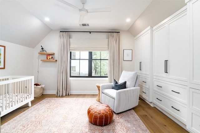 bedroom with ceiling fan, light hardwood / wood-style flooring, vaulted ceiling, and a nursery area