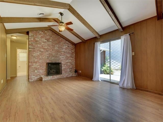 unfurnished living room with a brick fireplace, light hardwood / wood-style flooring, vaulted ceiling with beams, and wood walls