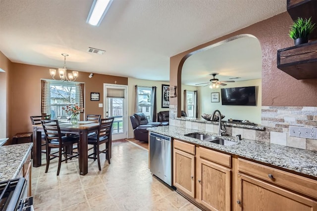 kitchen featuring stainless steel appliances, light stone counters, pendant lighting, ceiling fan with notable chandelier, and sink