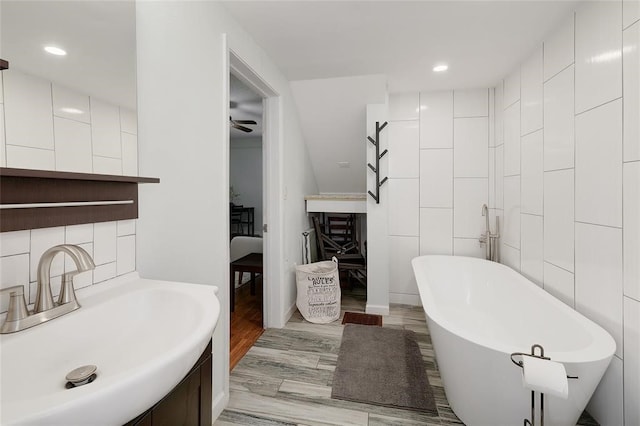 bathroom featuring wood-type flooring, a tub to relax in, tile walls, ceiling fan, and sink