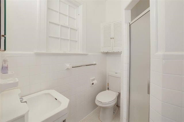 bathroom with tile walls, toilet, and a shower with door