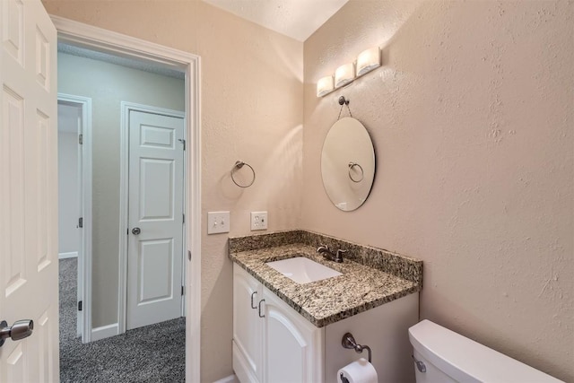 bathroom featuring toilet, a textured wall, and vanity