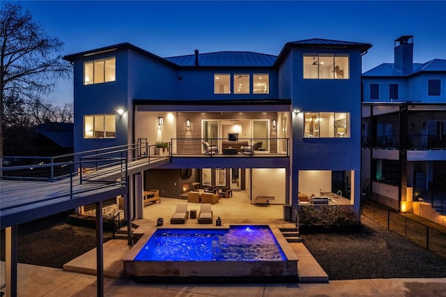 back house at dusk with a balcony, exterior kitchen, and an outdoor hangout area