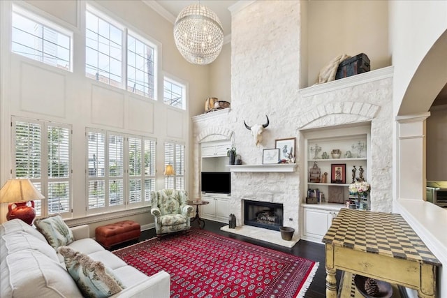 living room featuring an inviting chandelier, wood-type flooring, a stone fireplace, built in features, and ornamental molding