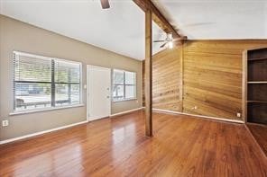 interior space featuring lofted ceiling with beams, hardwood / wood-style floors, wood walls, and ceiling fan