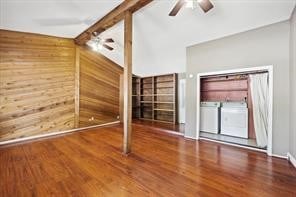 unfurnished living room featuring vaulted ceiling with beams, hardwood / wood-style flooring, separate washer and dryer, and wood walls