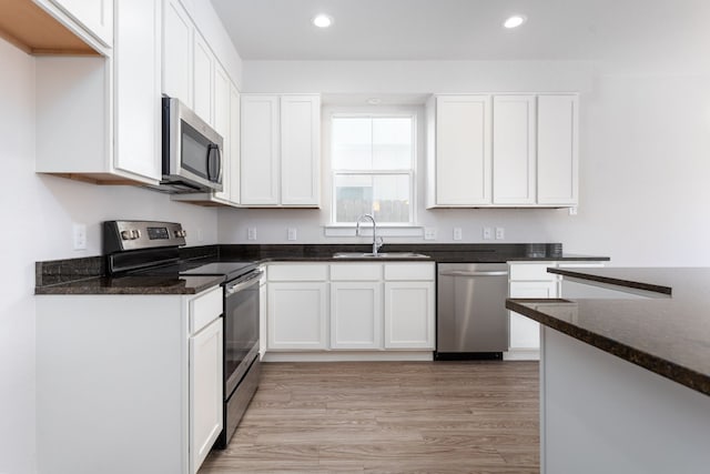 kitchen with dark stone countertops, white cabinetry, stainless steel appliances, and sink