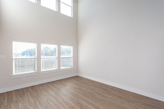 empty room featuring plenty of natural light, a high ceiling, and light hardwood / wood-style flooring