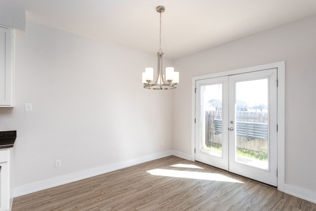 unfurnished dining area with hardwood / wood-style flooring, a chandelier, and french doors