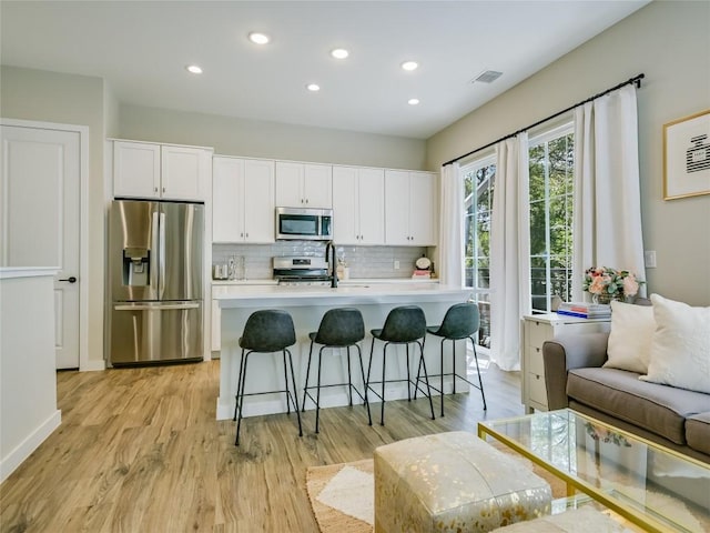 kitchen featuring a center island with sink, appliances with stainless steel finishes, white cabinets, and backsplash