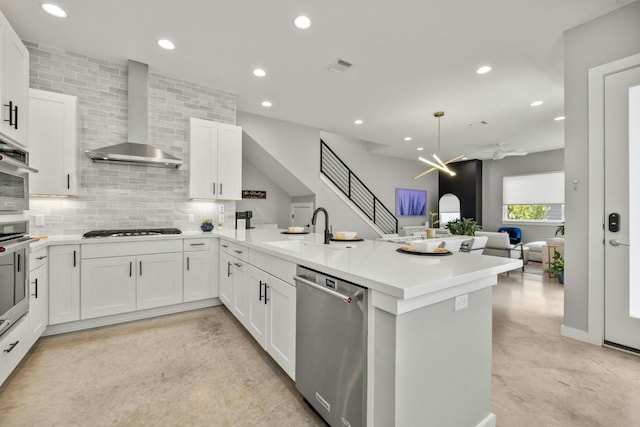 kitchen with wall chimney range hood, stainless steel appliances, white cabinets, and kitchen peninsula