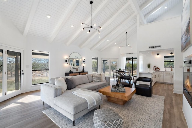 living room featuring visible vents, beam ceiling, wood finished floors, high vaulted ceiling, and a notable chandelier