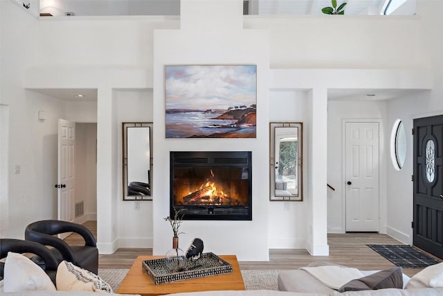 living area featuring visible vents, baseboards, light wood finished floors, a glass covered fireplace, and a high ceiling