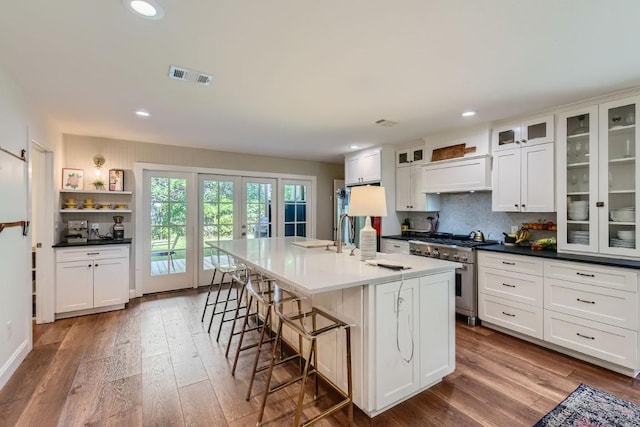 kitchen with an island with sink, white cabinets, high end stove, hardwood / wood-style floors, and custom exhaust hood