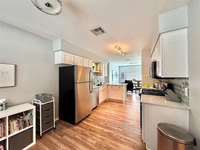 kitchen featuring kitchen peninsula, light hardwood / wood-style floors, sink, backsplash, and appliances with stainless steel finishes