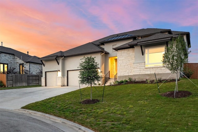 prairie-style home with a garage, fence, stucco siding, and stone siding