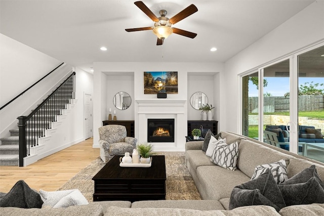 living area featuring recessed lighting, wood finished floors, stairs, a ceiling fan, and a lit fireplace