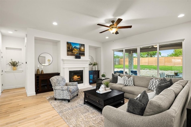 living room with recessed lighting, ceiling fan, light wood-type flooring, a glass covered fireplace, and baseboards