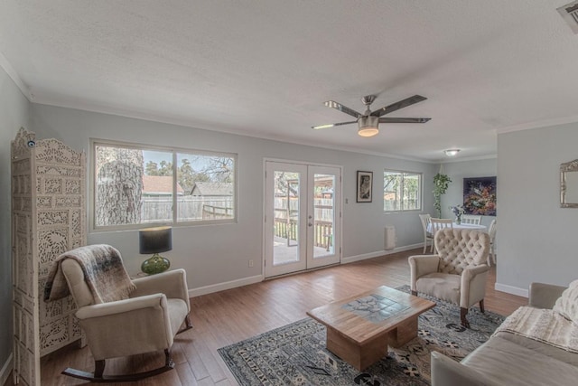 living room with a textured ceiling, baseboards, light wood-style floors, french doors, and crown molding