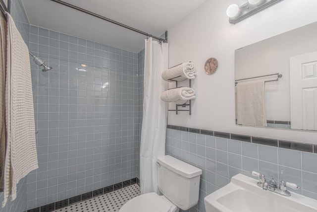 full bathroom featuring a wainscoted wall, tile walls, toilet, a sink, and a tile shower