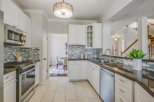 kitchen featuring appliances with stainless steel finishes, white cabinetry, ornamental molding, a sink, and glass insert cabinets