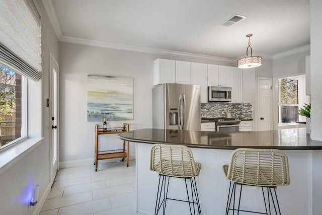 kitchen featuring white cabinets, decorative light fixtures, stainless steel appliances, a kitchen bar, and visible vents