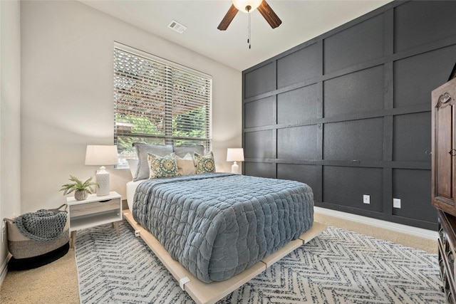 bedroom with a decorative wall, a ceiling fan, light colored carpet, and visible vents